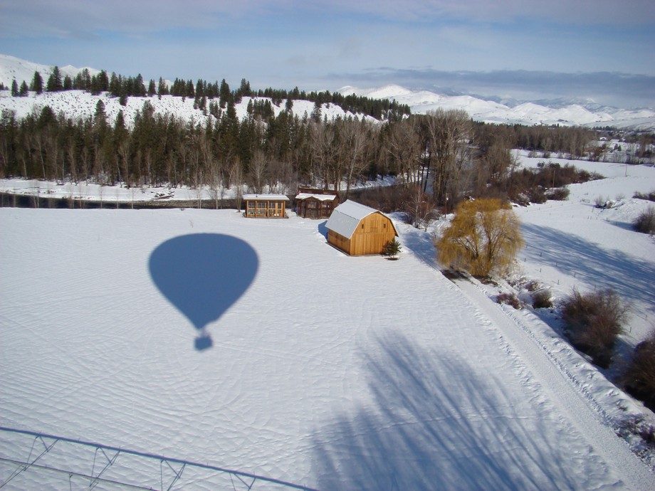 An arial view of a snow covered farm in Winthrop Washington. It's a bright day and you can see the shadow of the hot air balloon on the ground.